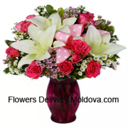 Roses roses et lys blancs avec des remplisseurs saisonniers dans un vase en verre